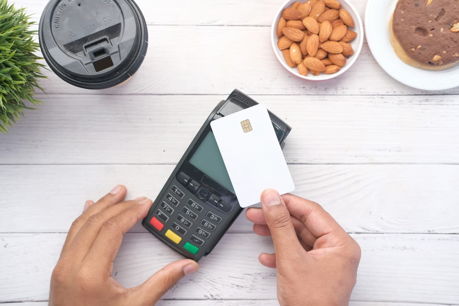 Une main tient une carte de paiement à côté d'une calculatrice posée sur un bureau.
