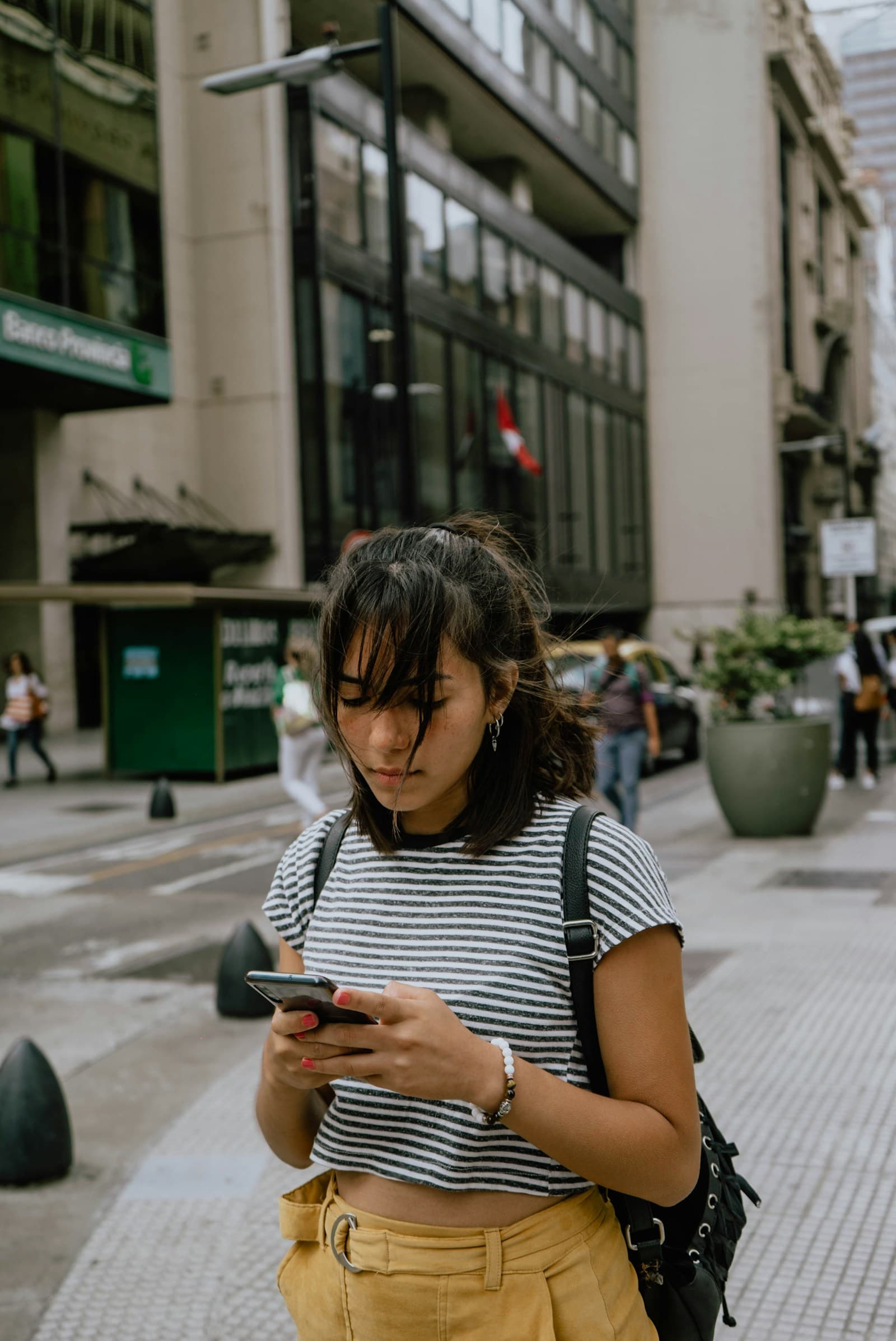 Une femme consulte son téléphone dans la rue, adossée à un mur.