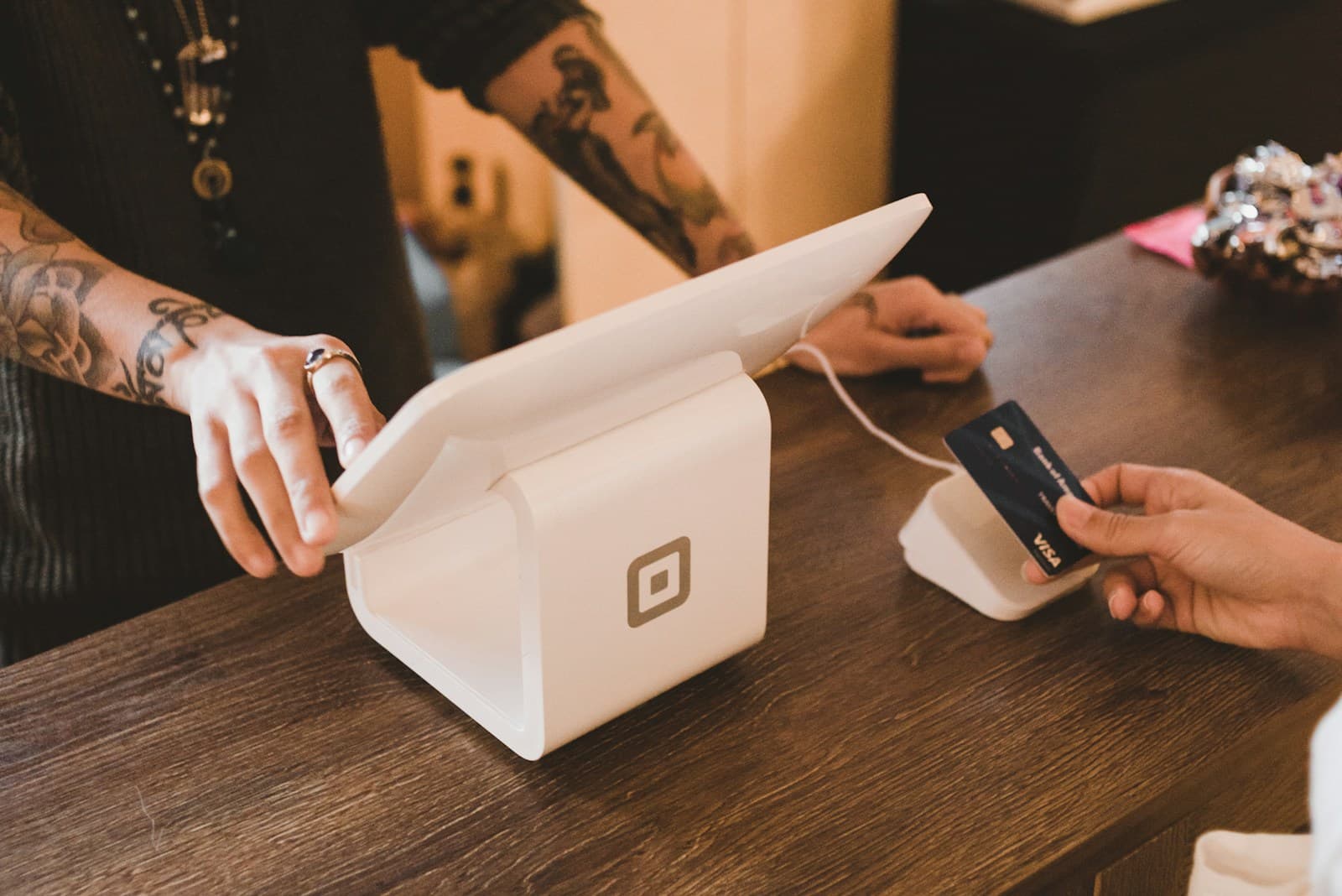 Une personne tend un terminal de paiement blanc pour encaisser un règlement par carte.