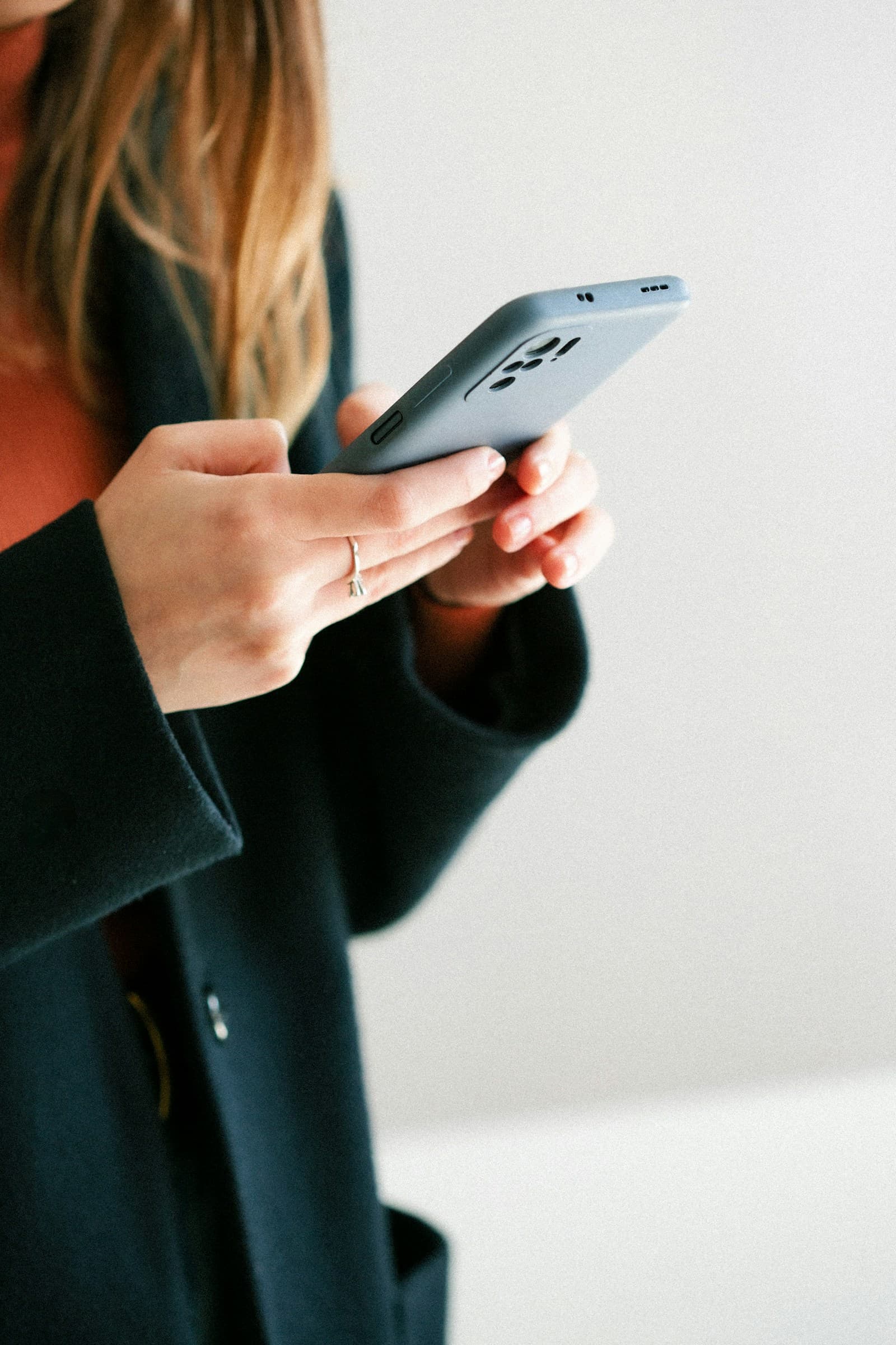 Une femme tient son téléphone à deux mains, le regard attentif sur l'écran.