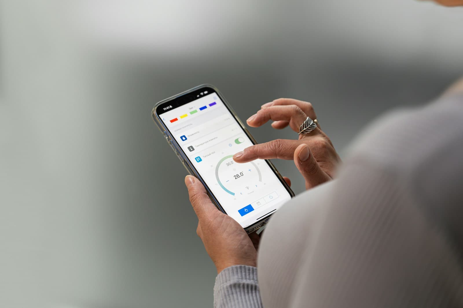 Deux mains tenant un téléphone dont l'écran affiche une application, posées au-dessus d'un bureau clair.