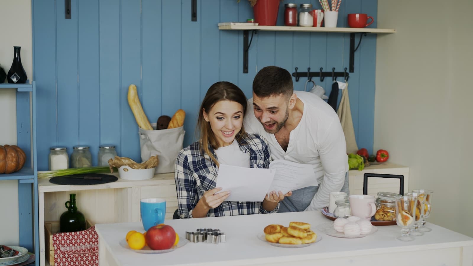 Un couple debout dans une cuisine lumineuse lit un courrier ensemble.
